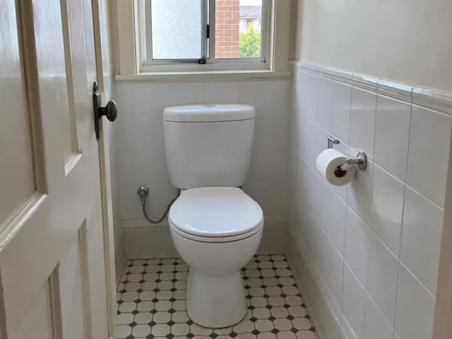 Clean white toilet in a small tiled bathroom with a window and patterned floor in Cabramatta