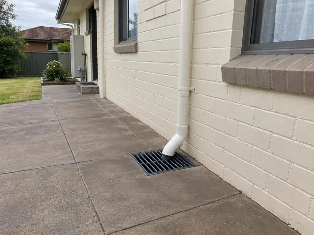 Concrete patio with a seated stormwater grate beside a house wall and downpipe in Canley Heights